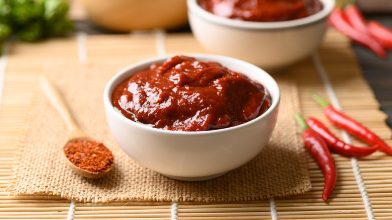 A bowl of gochujang next to chiles and dried spices