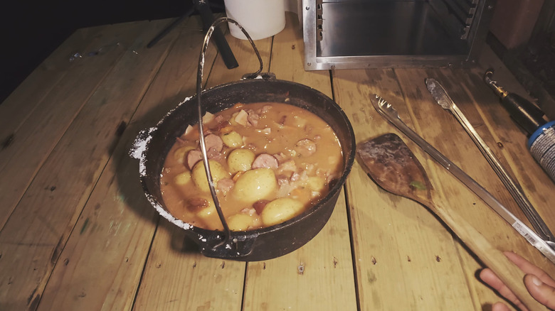Someone places a serving spoon next to a cast iron pot of son of a gun stew.