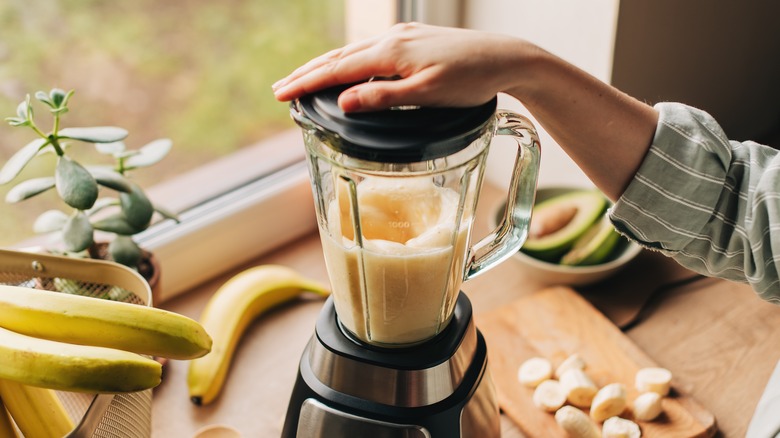 Person blending a smoothie next to a window