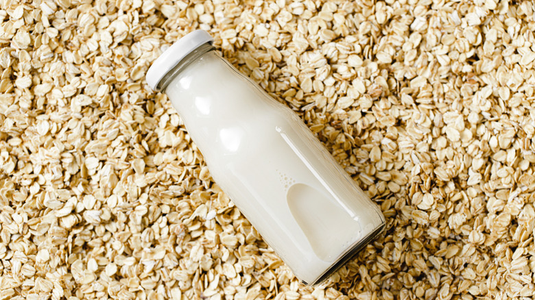Glass bottle of oat milk laid on top of oats
