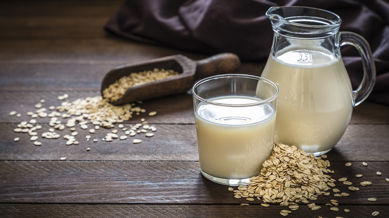 Oat milk in glass and jug next to pile of oats