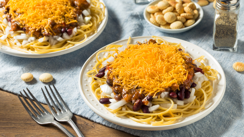 Plate of Cincinnati chili with chili, beans, onions, and cheese with oyster crackers and another plate in the background