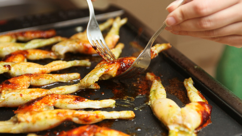Grilled frog legs being lifted with forks