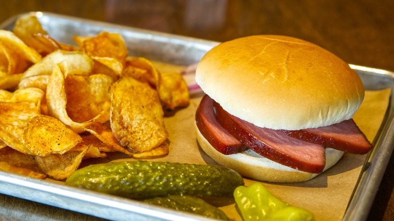Smoked bologna on a sandwich with chips and a pickle