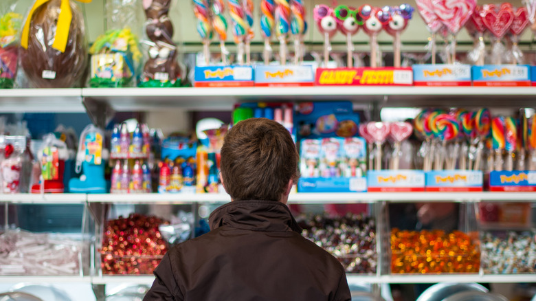 Child in brown jacket faces shelves of assorted candies
