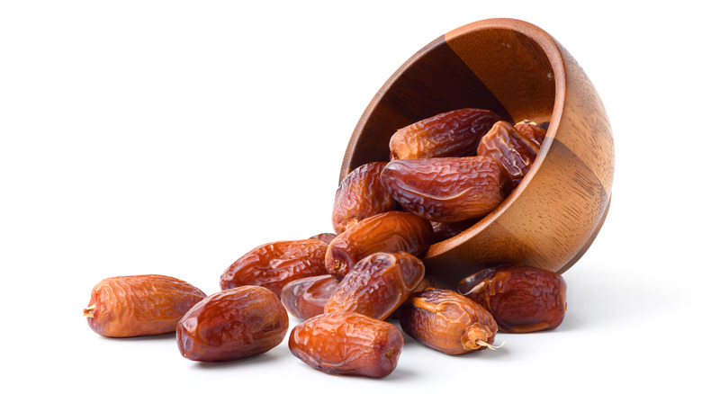Dried dates spilling out of a tipped over wooden bowl