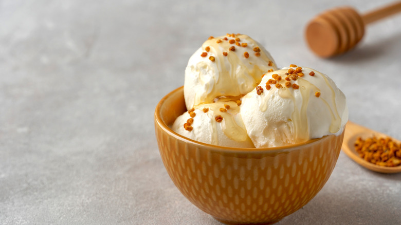 Honey drizzled over ice cream with a crunchy topping near a honey dipper