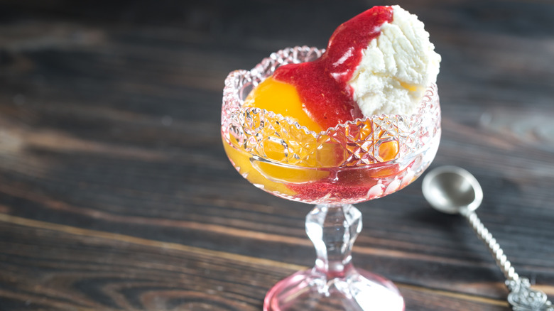 Crystal dish of Peach Melba beside a silver spoon atop dark wood