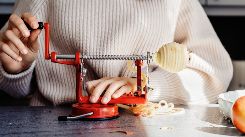 Woman operating a hand-turn apple peeler