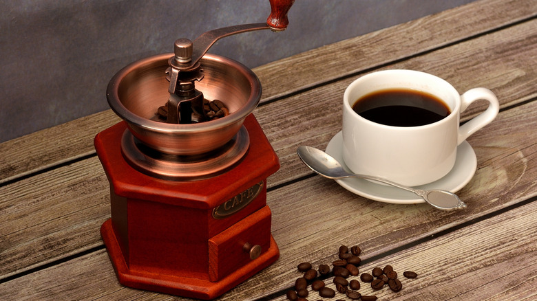 Vintage coffee grinder next to a cup of black coffee