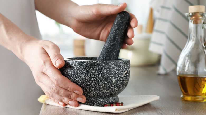 Person utilizing a mortar and pestle on wood counter