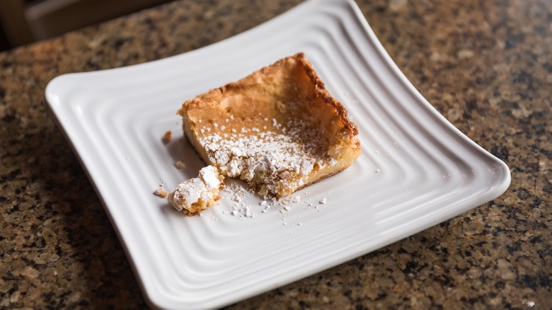Decorative plate with a crumbling corner piece of gooey butter cake, dusted with powdered sugar