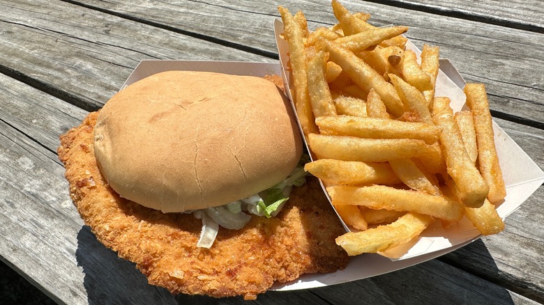 Pork tenderloin sandwich served on a bun with French fries atop a picnic table