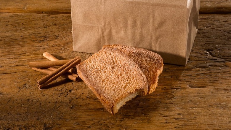 Slices of Trenary toast beside cinnamon sticks in front of a brown paper bag