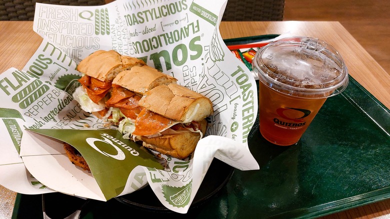 Unwrapped Quiznos sub served up on a platter with a drink and side