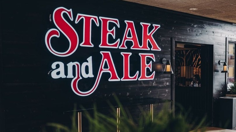 Prominent red and white sign on dark background denoting entryway of Steak and Ale