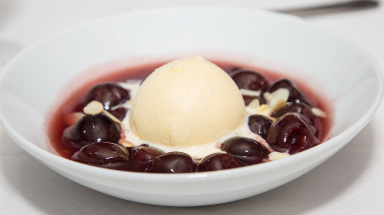 Cherries jubilee in a white bowl with vanilla ice cream