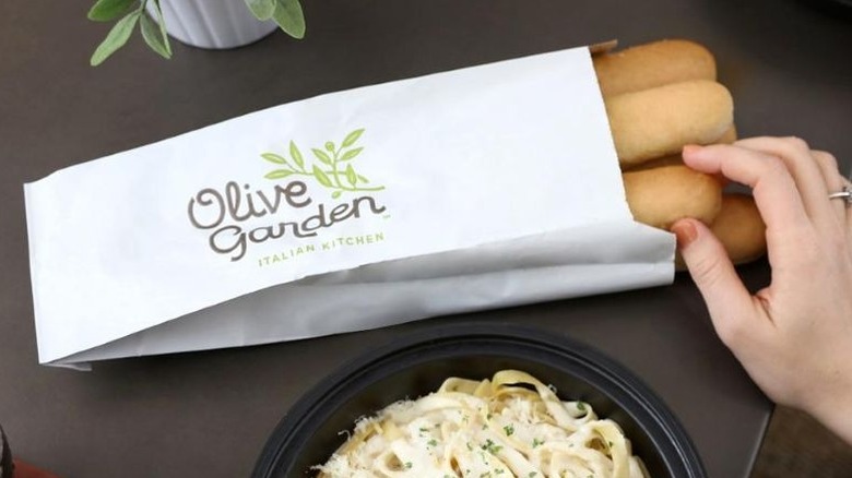 Hand taking breadsticks out of an Olive Garden bag