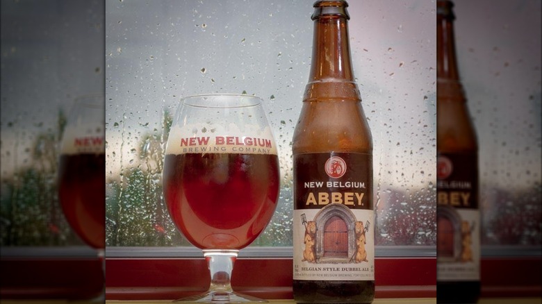 A glass and a bottle of New Belgium Abbey beer in front of a window with rain outside