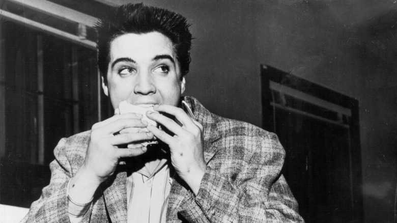 Black-and-white photo of a young Elvis Presley biting into a sandwich