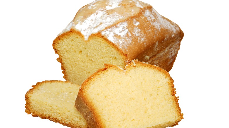 A loaf of pound cake, with two slices cut away, against a white background
