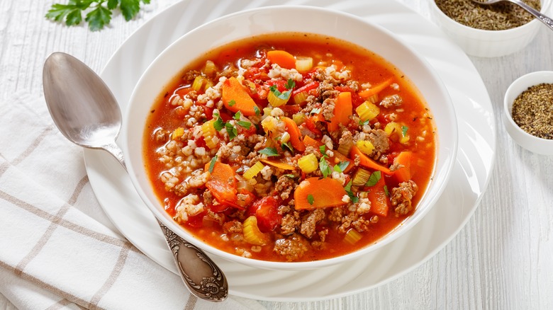 Hamburger soup with vegetables and barley in a red broth in a white bowl