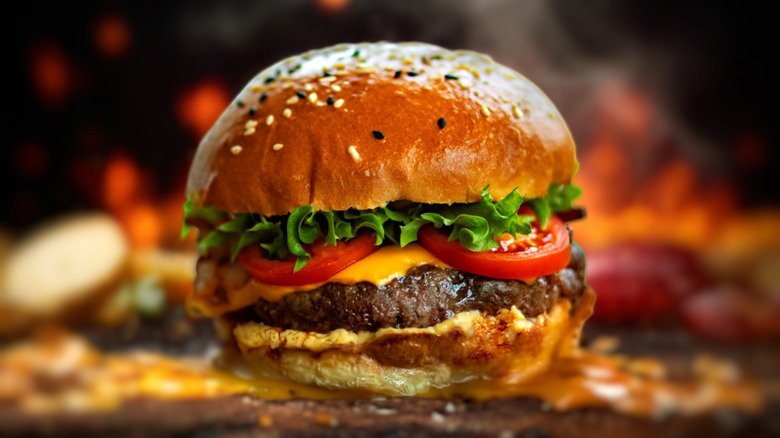Classic cheeseburger with meat patty, sliced tomatoes, lettuce, and cheese on a seed-speckled hamburger bun