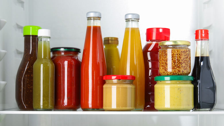 Assortment of colorful condiments in unlabeled jars on refrigerator shelf