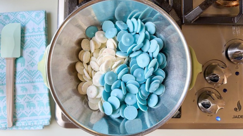 Pastel blue and cream candy melts in stainless steel bowl over saucepan double boiler