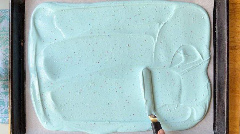 Spreading melted pastel candy melts onto parchment-lined baking sheet with offset spatula