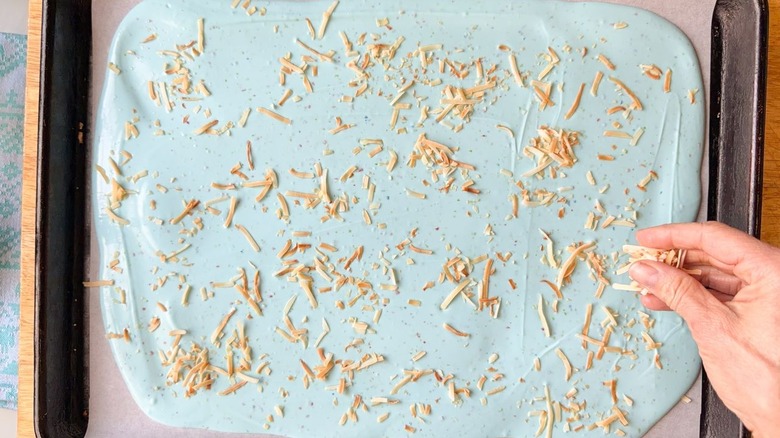 Sprinkling toasted coconut onto pastel blue Easter bark on sheet pan
