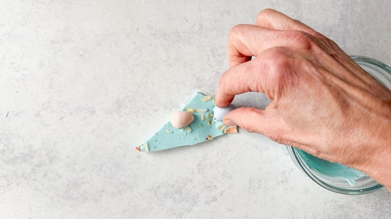 Attaching candy-coated chocolate eggs to pastel blue Easter bark piece with melted candy