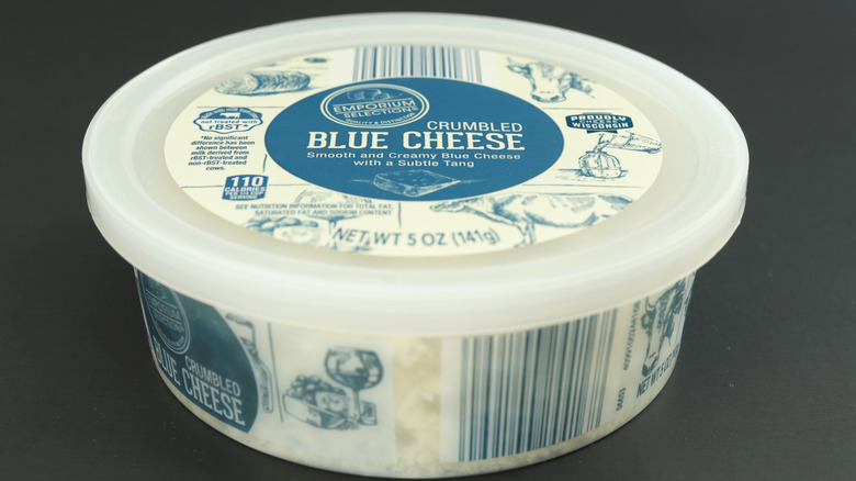 Container of Emporium Selection crumbled blue cheese isolated against dark background