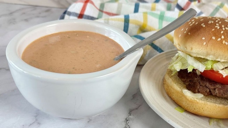 Bowl of burger sauce next to burger on plate