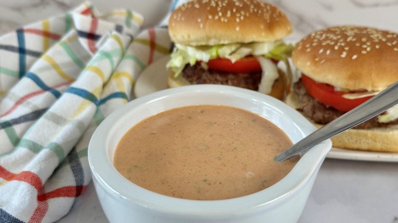 Bowl of burger sauce in front of two burgers
