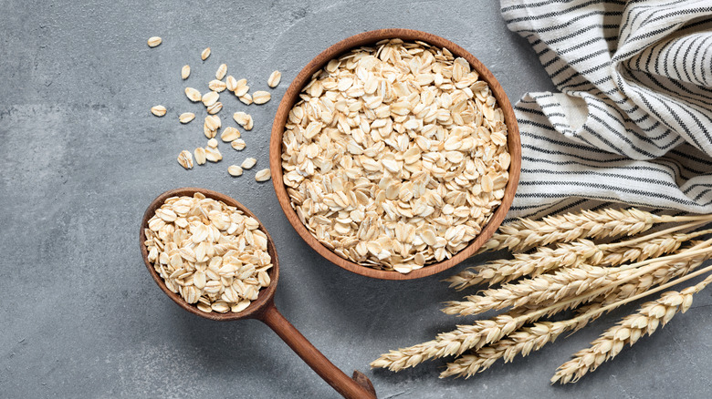 A bowl of oats along with a spoon, a dishtowel, and a few stalks of oats