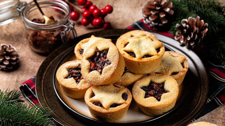 A plate of baked mince pies with star cut outs in the top of the dough are stacked on top of each other