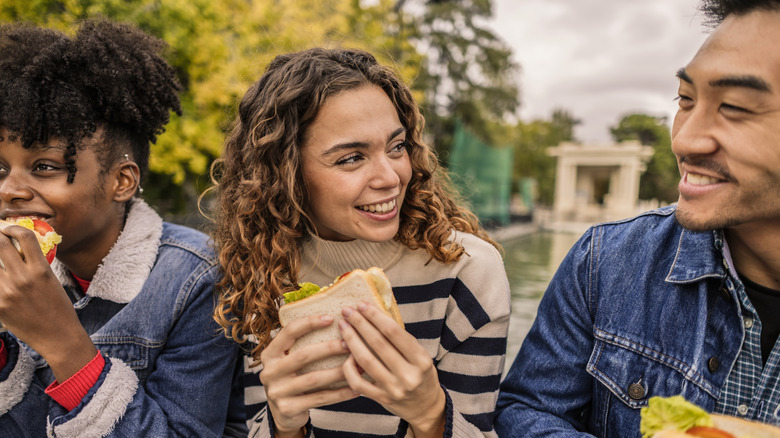 Three friends sitting and enjoying sandwiches together