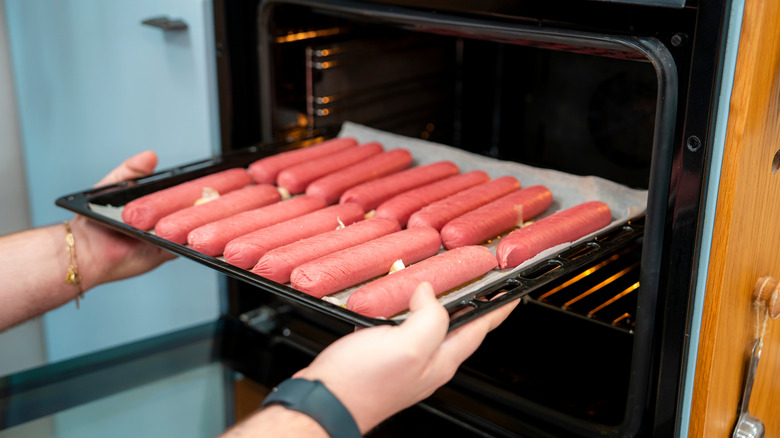 Two rows of hot dogs being placed into the oven