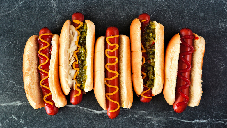 Five hot dogs in buns covered with toppings