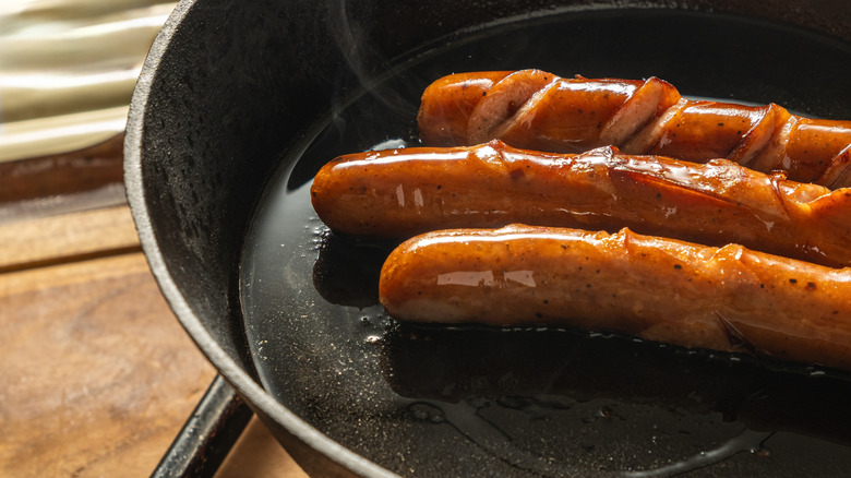 Hot dogs cooking in a cast iron pan