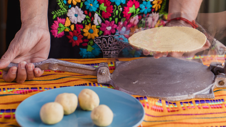 Person pressing maize dough with tortilla press