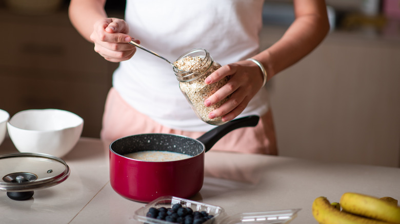 Person putting oats in a pot of milk