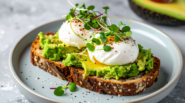 A slice of avocado toast with poached eggs, pepper, and microgreens