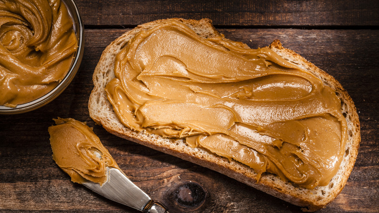 A slice of toast has a generous helping of peanut butter smeared on it,
