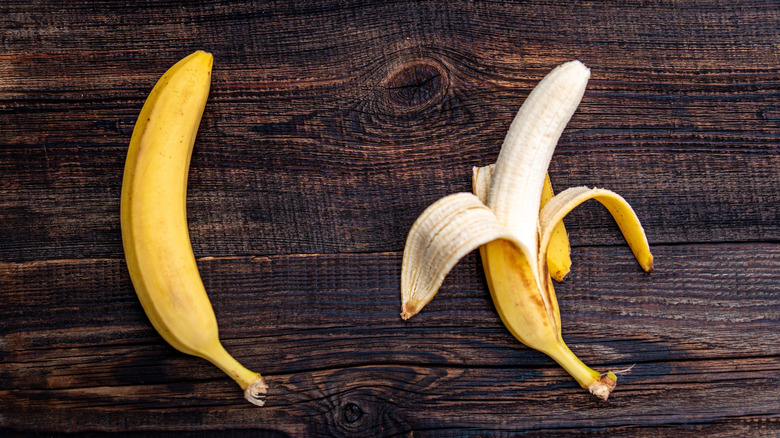 An unpeeled banana next to a banana peeled from the bottom