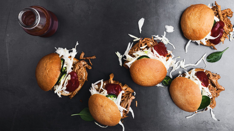 Top view of various pulled pork sliders and barbecue sauce