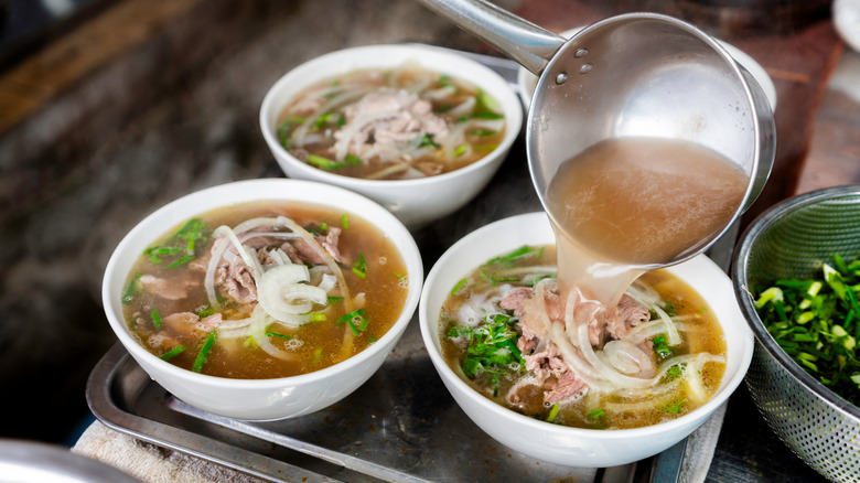 Broth being poured into a bowl of pho with two other bowls on a tray