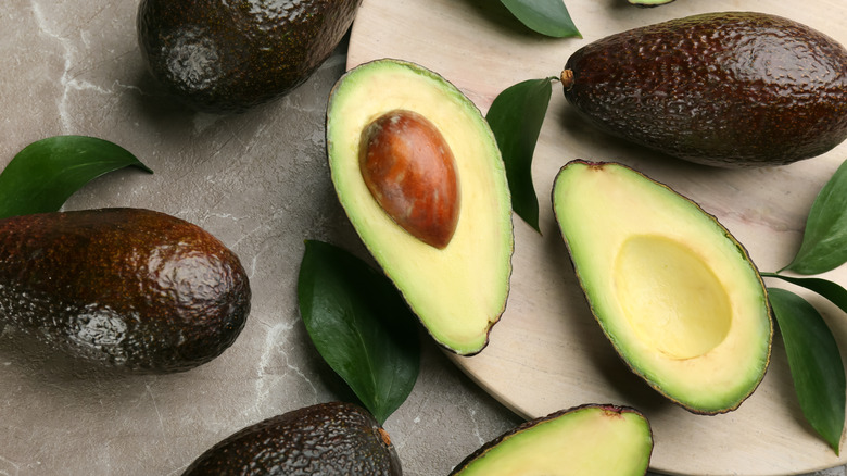 Halved avocado next to whole avocados
