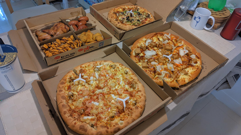 Various Pizza Hut pizzas in their boxes next to fried food like wings and fried pickles.